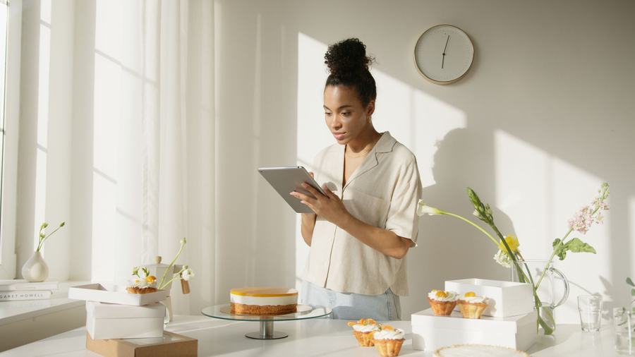 Bakery owner checking orders on a tablet in a sunlit kitchen