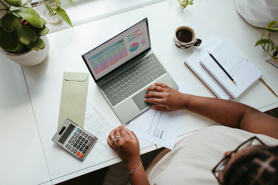 Bookkeeping spreadsheet on a laptop beside a calculator and notebook
