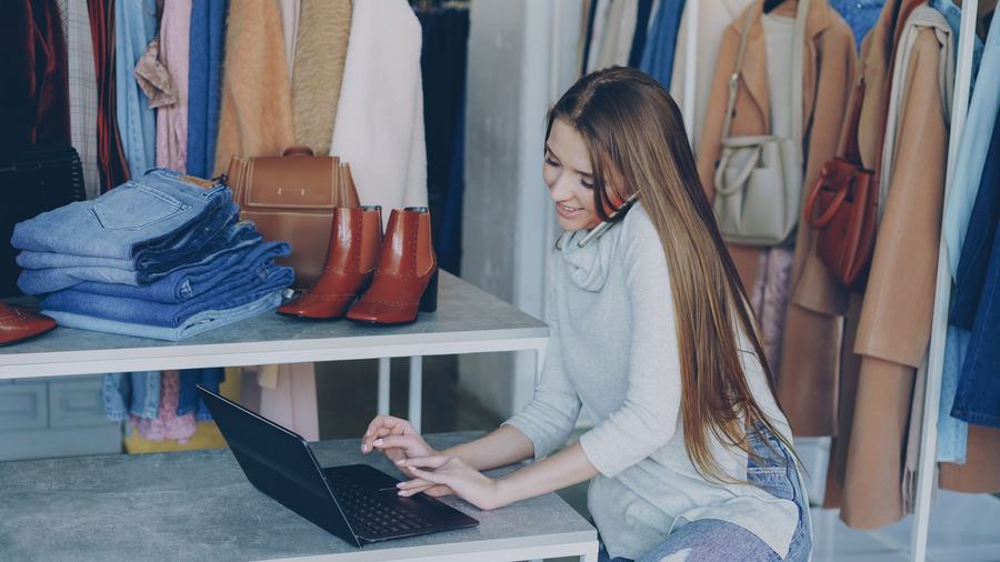 Boutique owner working on a laptop beside shelves of clothing