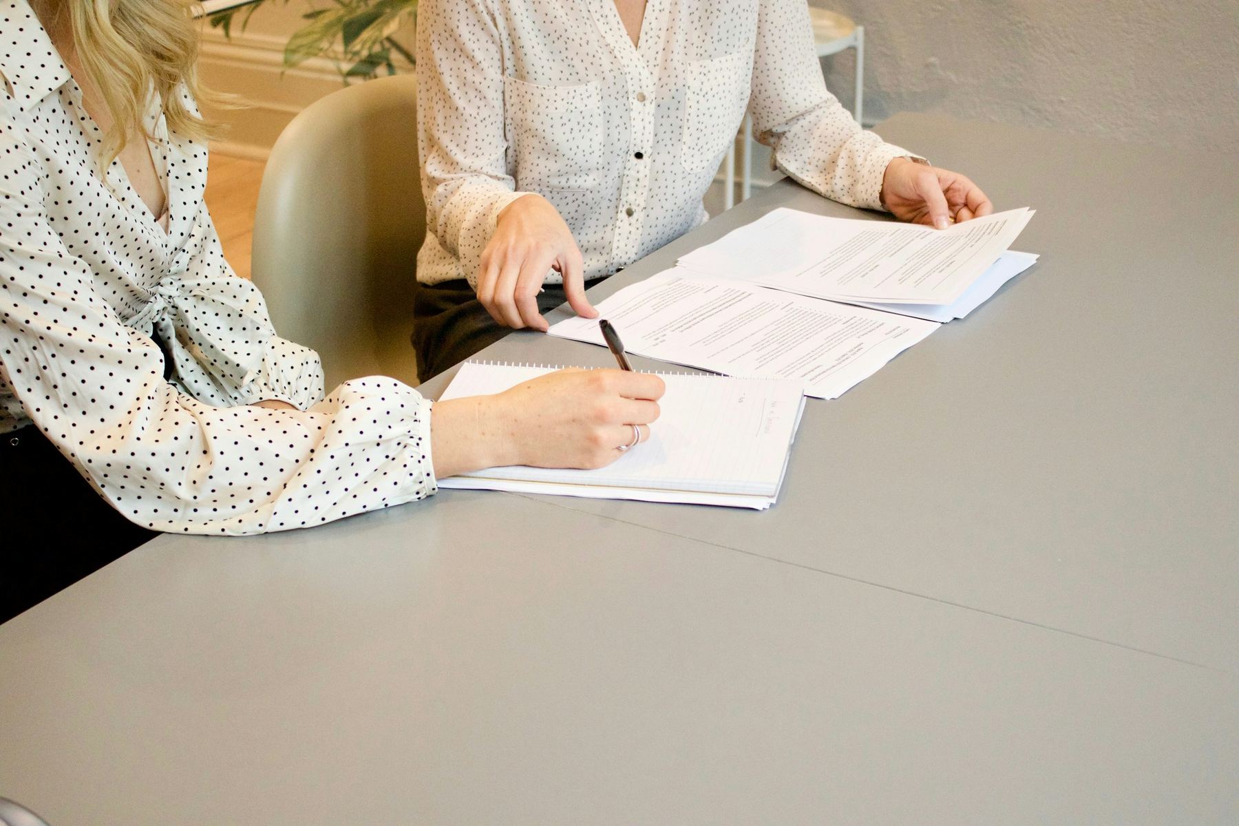 Two people at a grey table, one signing a document